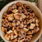 A tan bowl of sourdough snack mix on a wooden board with greenery and red berries. Made in the kitchen at Nystrom Orchard in Worthington Minnesota.