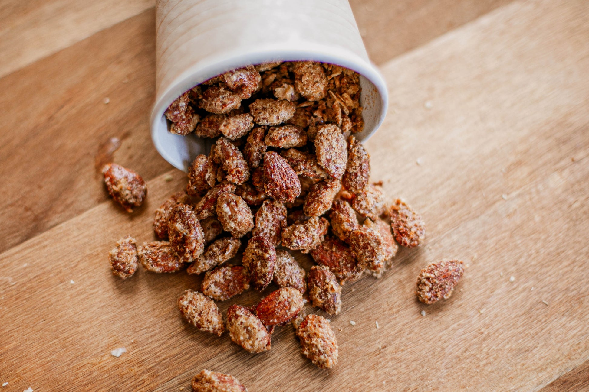 Spiced toasted almonds spilling out of a white cup on a wooden cutting board. Made by the kitchen at Nystrom Orchard in Worthington Minnesota. 