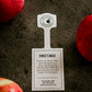 A SweeTango apple with a label, showing the brand name and some information, placed on a dark surface with other apples around. Picked in Nystrom Orchard in Worthington Minnesota.