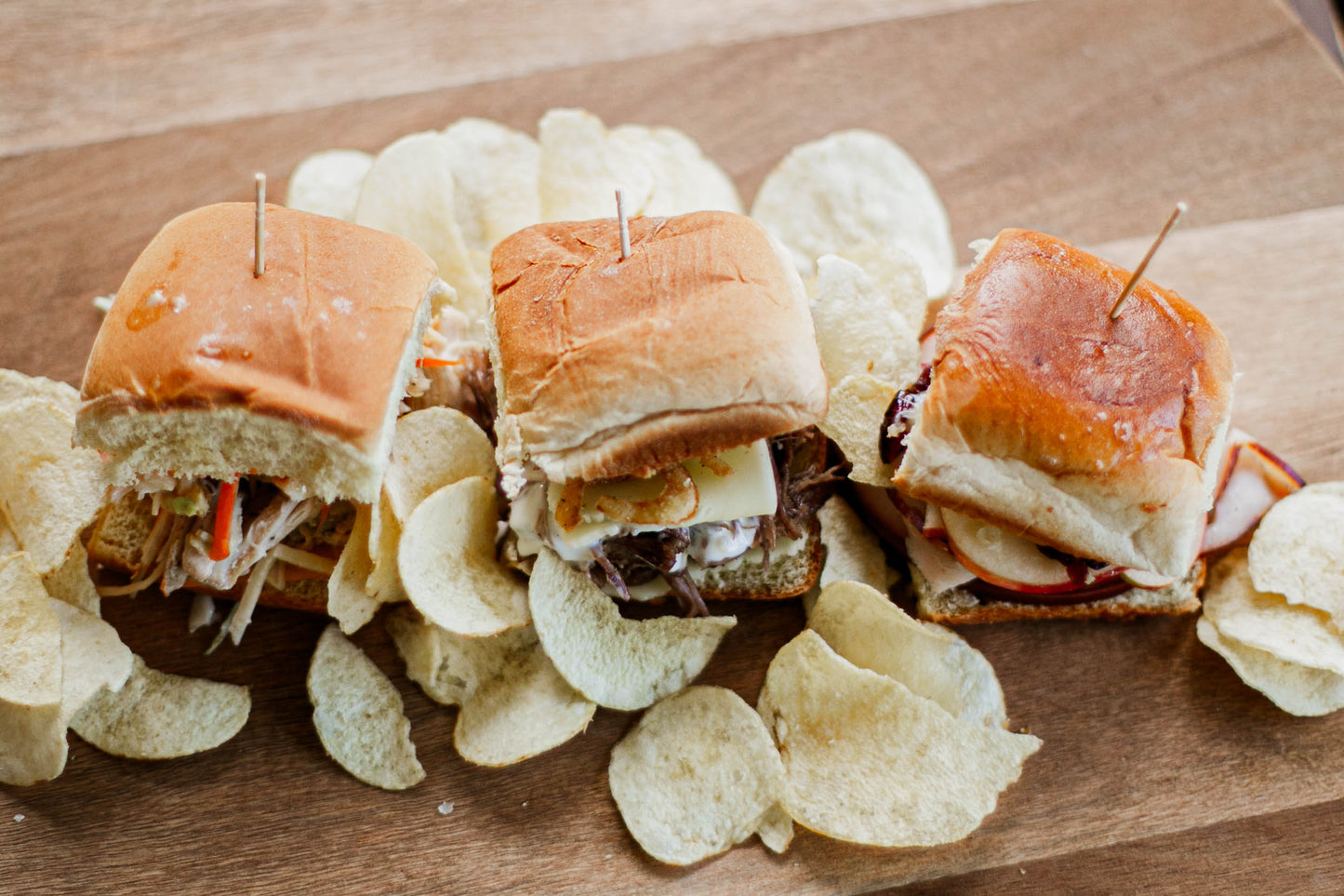 3 sliders with different fillings on a wooden board with potato chips. Made in the kitchen of Nystrom Orchard in Worthington Minnesota.