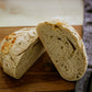 Sliced loaf of rustic white cheddar dill sourdough bread on a wooden cutting board with a knife and cloth in the background. Made in the kitchen of Nystrom Orchard in Worthington Minnesota. 