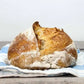 A loaf of rustic homemade sourdough bread on a blue striped towel on a table. The bread is baked in the kitchen at Nystrom Orchard in Worthington Minnesota. 