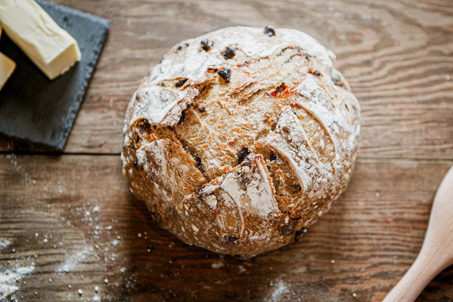 Artisan loaf of sourdough white chocolate almond bread on a rustic wooden surface with butter and a wooden spoon on the side. Baked in the kitchen at Nystrom Orchard in Worthington Minnesota. 