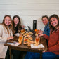 Four women sitting around a table with cider flights and food, smiling at the camera. Event hosted by Nystrom Orchard in Worthington Minnesota.