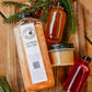 Bottle of cold pressed apple cider and cider syrup with salted caramel on a wooden board with greens and red berries. Made in the kitchen at Nystrom Orchard in Worthington Minnesota. 