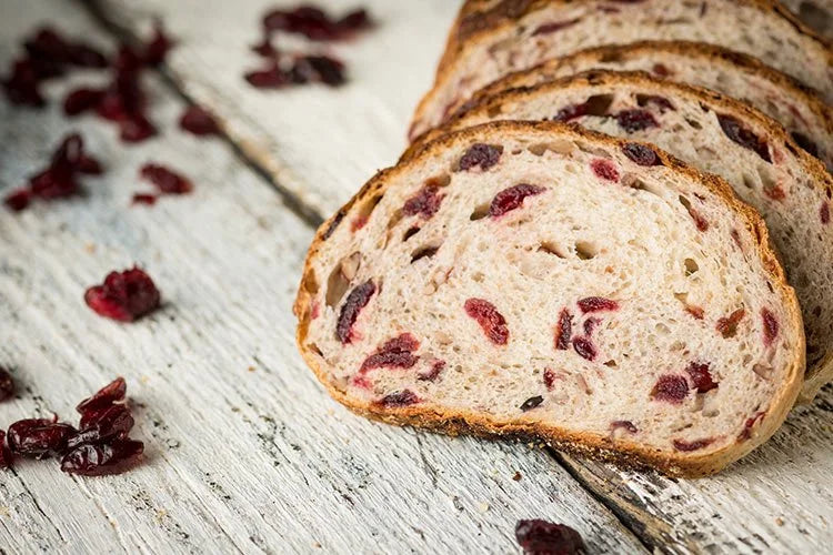 Rustic sourdough cranberry glazed pecan bread sliced on a wooden surface with cranberries scattered around. Baked in the kitchen at Nystrom Orchard in Worthington Minnesota.