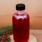 Bottle of cranberry vanilla syrup on a wooden surface with greenery and red berries. Made in the kitchen at Nystrom Orchard in Worthington Minnesota.