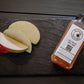 Photo of apple slices and a single serve bottle of cold pressed cider on a slate on a dark background. Pressed in the kitchen of Nystrom Orchard in Worthington Minnesota.