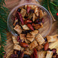 Maple pecan snack mix with nuts and raisins and rice chex in a cup on a wooden board with greenery. Made in the kitchen at Nystrom Orchard in Worthington Minnesota.