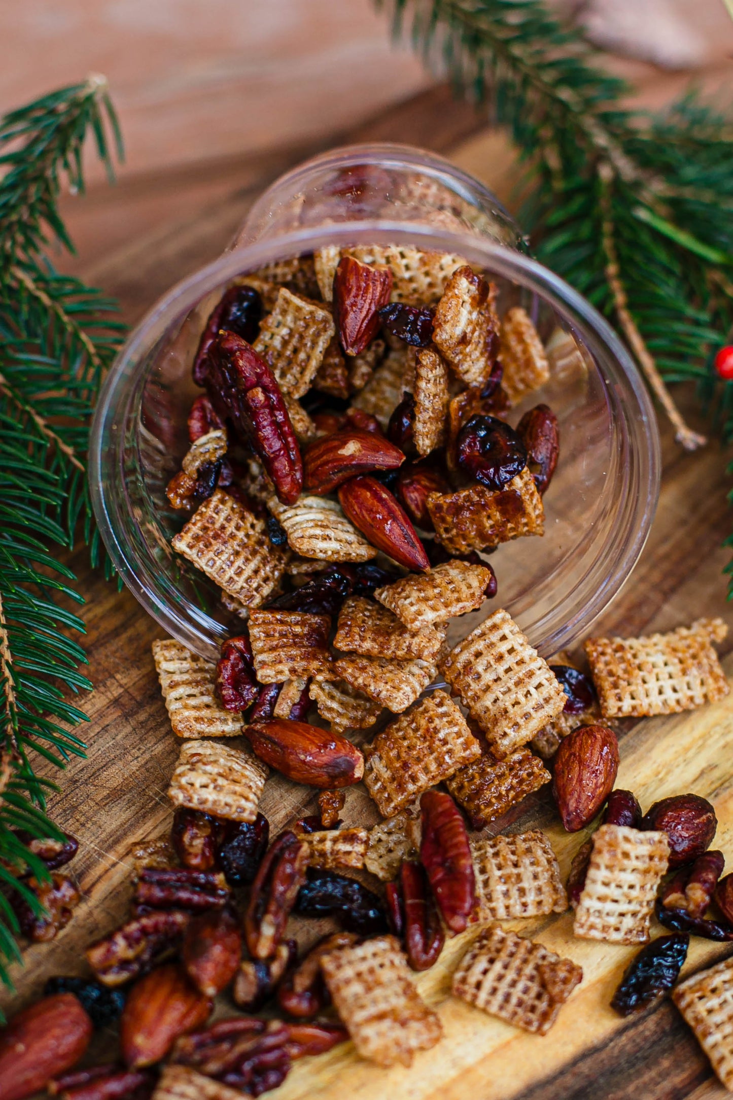 Maple pecan snack mix with nuts and raisins and rice chex in a cup on a wooden board with greenery. Made in the kitchen at Nystrom Orchard in Worthington Minnesota.