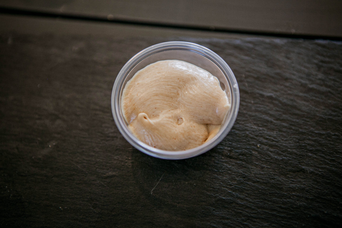 Top view of a 2 oz. container of peanut butter dip on a dark surface. Made in the kitchen of Nystrom Orchard in Worthington Minnesota.