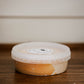 8 oz apple pie dip topped with salted caramel in a clear deli container with a lid on a wooden surface with a white background. Made in the kitchen of Nystrom Orchard in Worthington Minnesota.