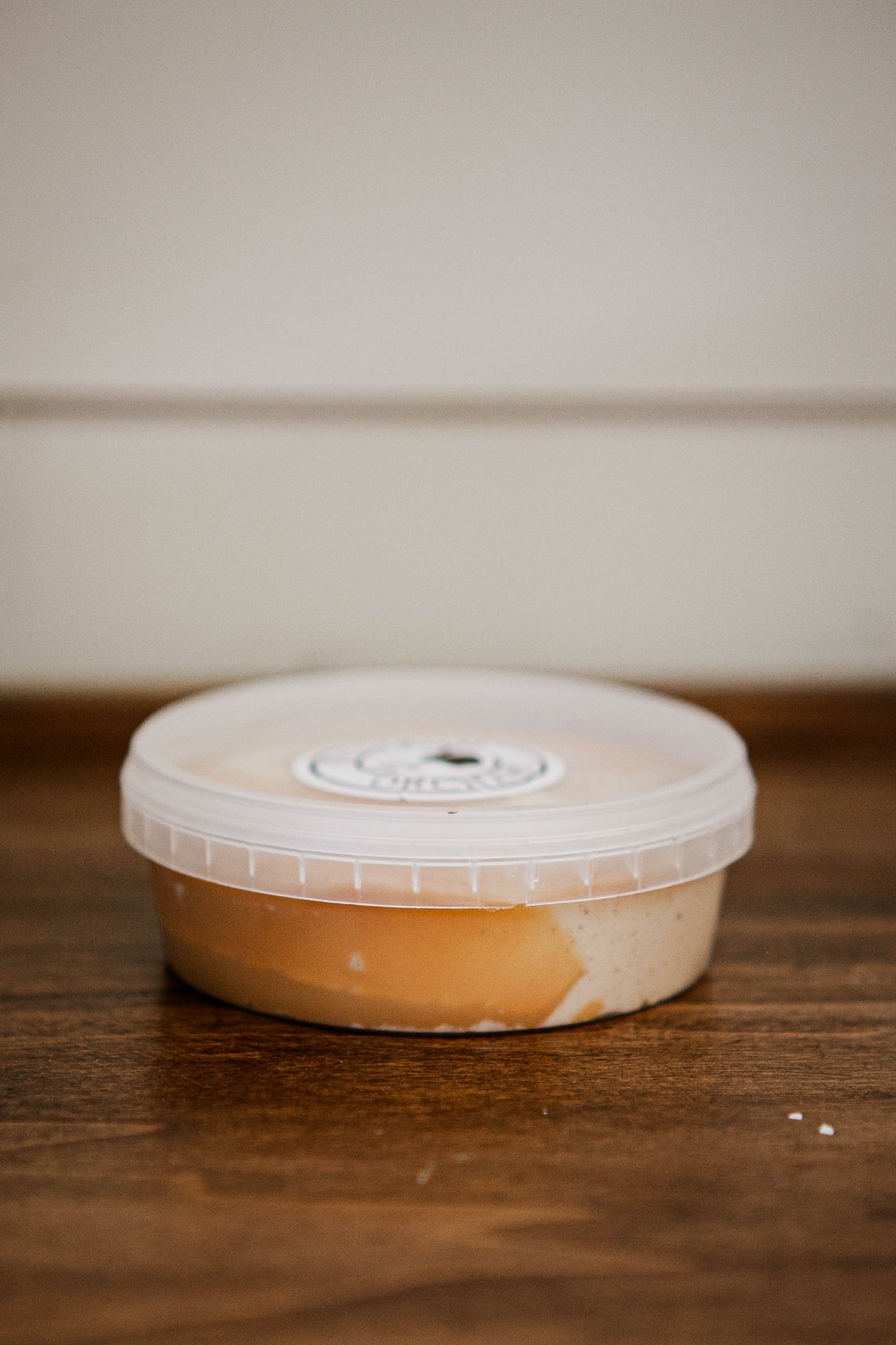 8 oz apple pie dip topped with salted caramel in a clear deli container with a lid on a wooden surface with a white background. Made in the kitchen of Nystrom Orchard in Worthington Minnesota.