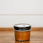 Small jar of caramel sauce on a wooden surface with a white background. Made in the kitchen at Nystrom Orchard in Worthington Minnesota.