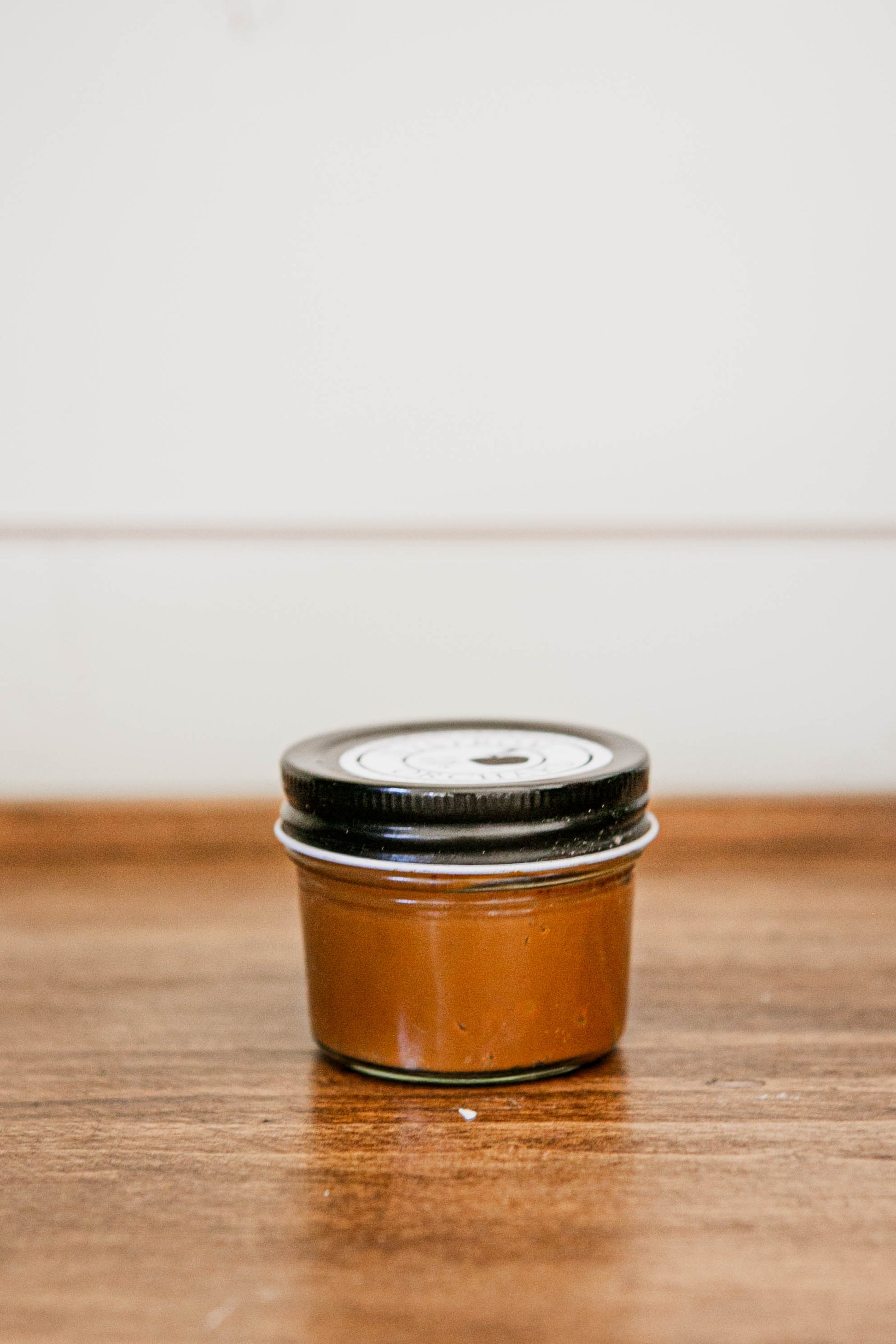 Small jar of caramel sauce on a wooden surface with a white background. Made in the kitchen at Nystrom Orchard in Worthington Minnesota.