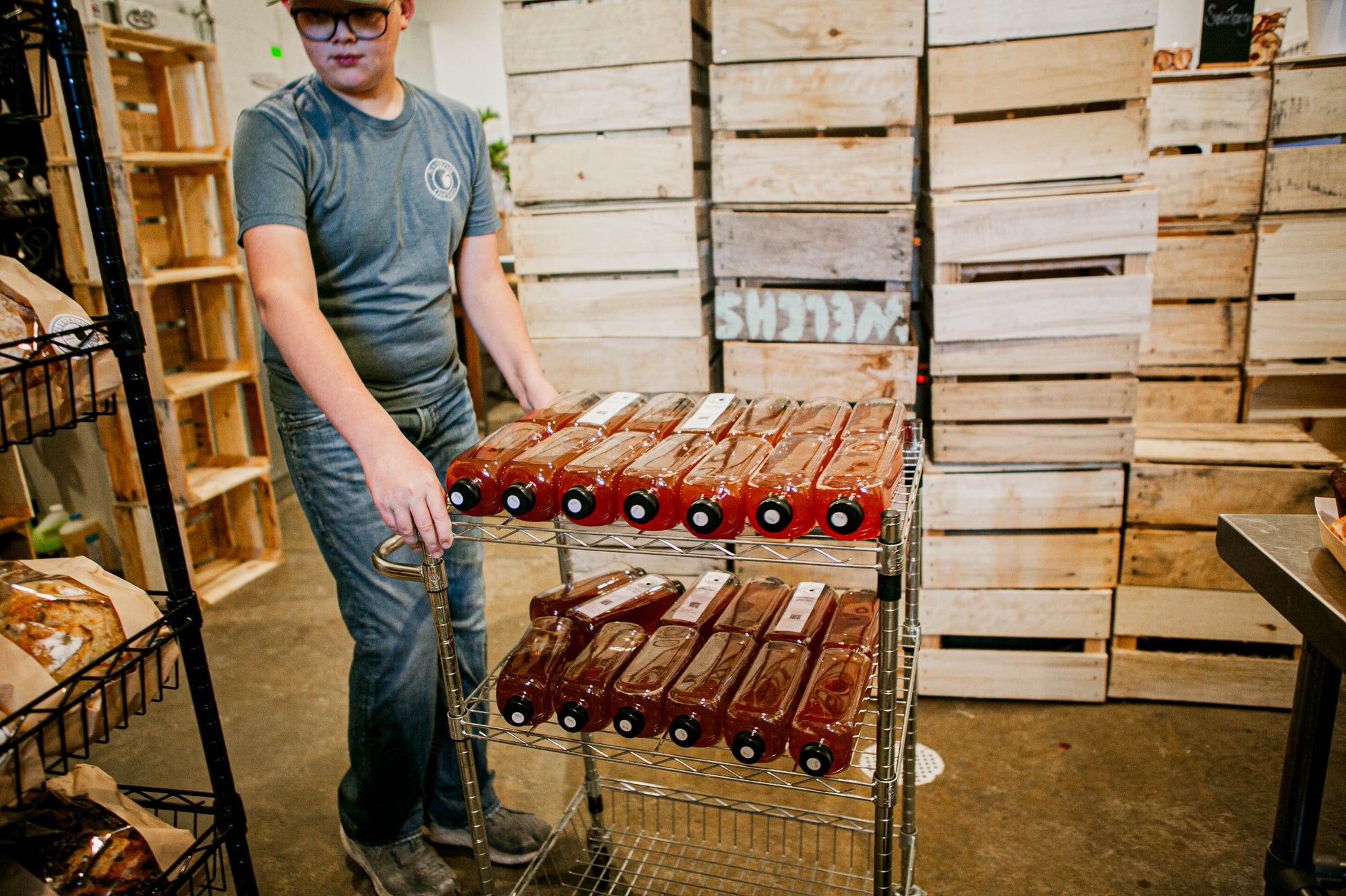 Person pushing a cart full of cold pressed cider ready to stock shelves in a room full of apple crates. Sold in the store of Nystrom Orchard in Worthington Minnesota.