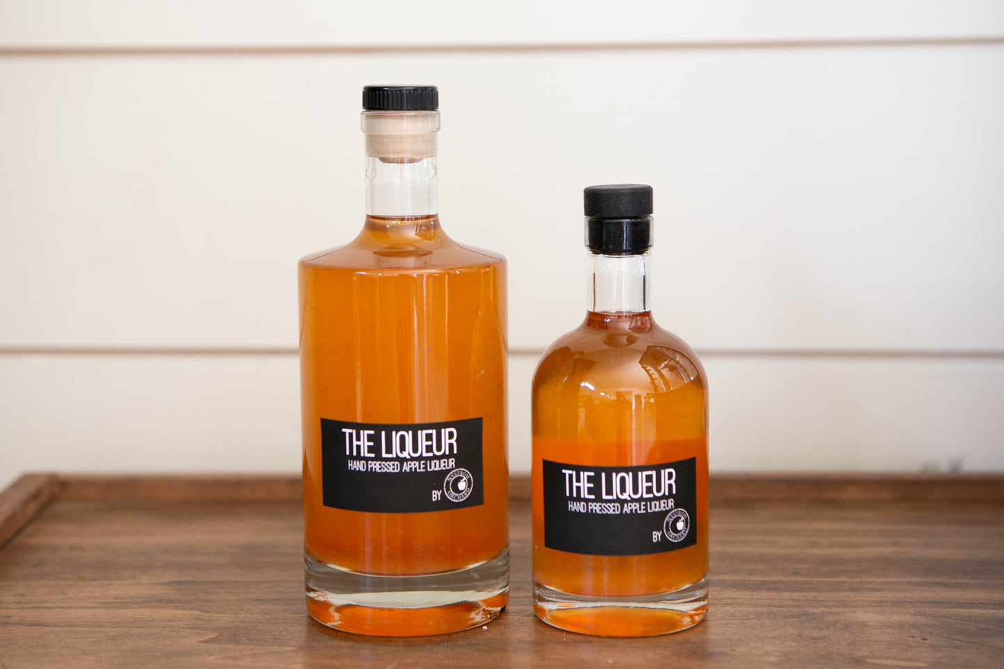 Two glass bottles of apple liqueur on a wooden table with a white background. Made in the kitchen of Nystrom Orchard in Worthington Minnesota. 