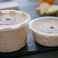 A 16 oz. and 8 oz. container of peanut butter dip with lids on a dark surface with a blurry background. Made in the kitchen of Nystrom Orchard in Worthington Minnesota