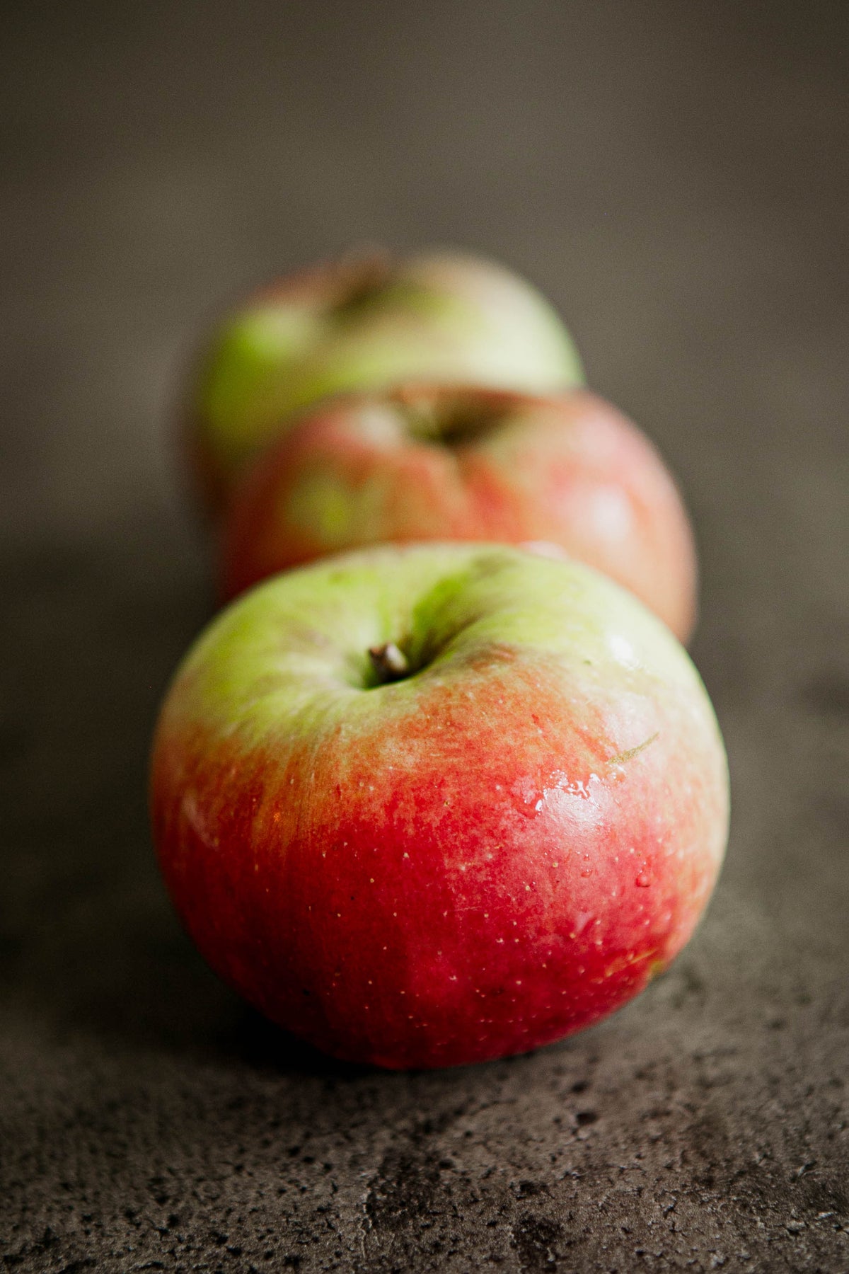A row of 3 Wealthy apples on a concrete surface. Picked in Nystrom Orchard in Worthington Minnesota.