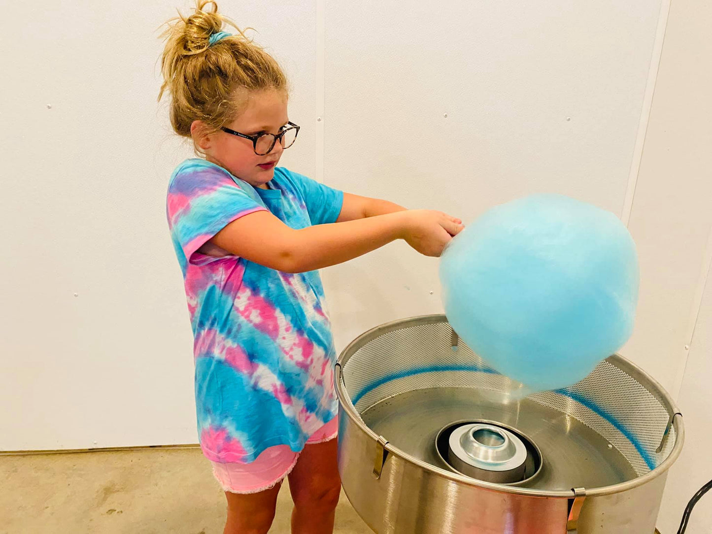 Girl making cotton candy with a machine with white walls in the background. Made in the kitchen of Nystrom Orchard in Worthington Minnesota.