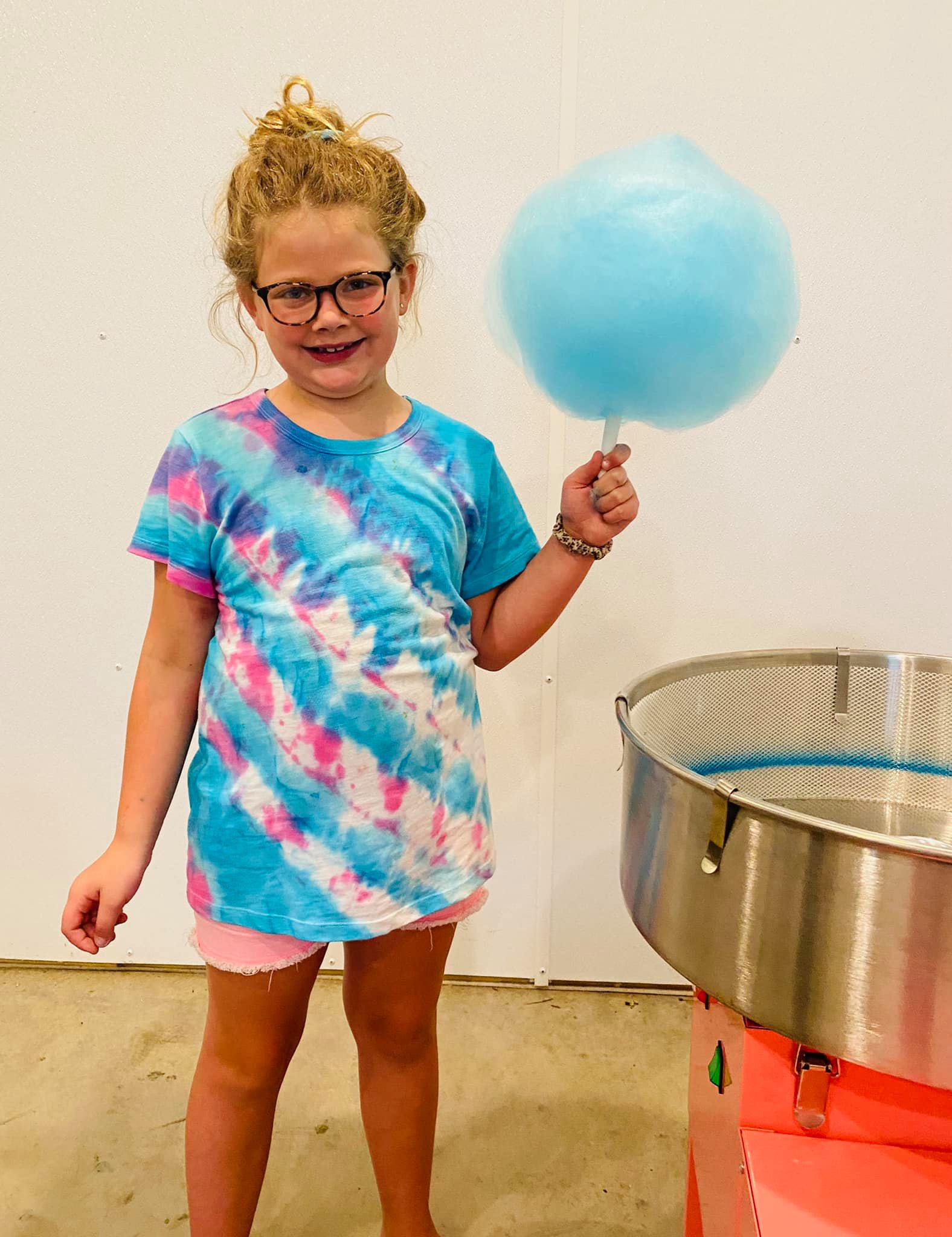 Girl holding cotton candy standing beside a cotton candy machine with a white background. Made in the kitchen of Nystrom Orchard in Worthington Minnesota.