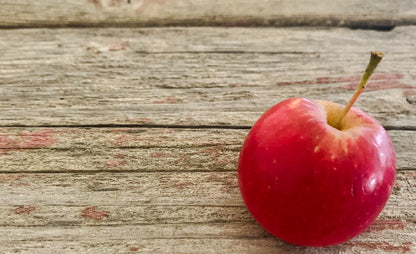 A single red crab apple placed on a wooden surface with a rustic appearance. Picked in Nystrom Orchard in Worthington Minnesota.