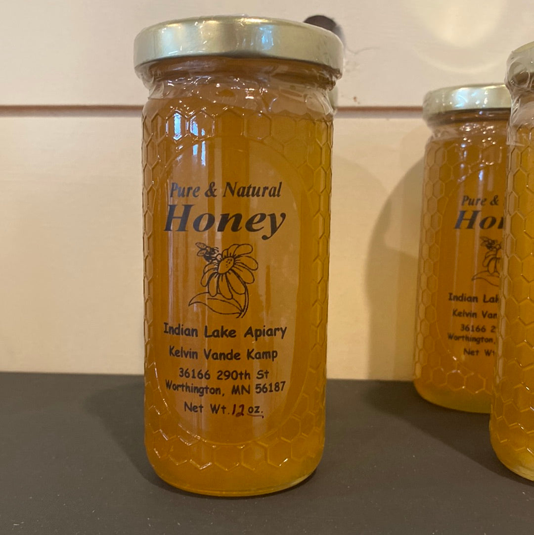 Pure natural honey in a 12 oz jar with a couple jars behind on a dark surface with a white background. Sold by Nystrom Orchard in Worthington Minnesota.