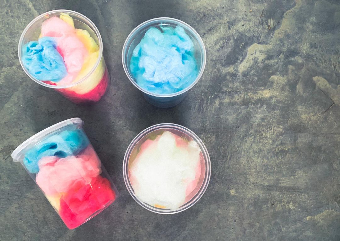 Four containers of cotton candy with varying colors placed on a textured surface. Made in the kitchen of Nystrom Orchard in Worthington Minnesota.