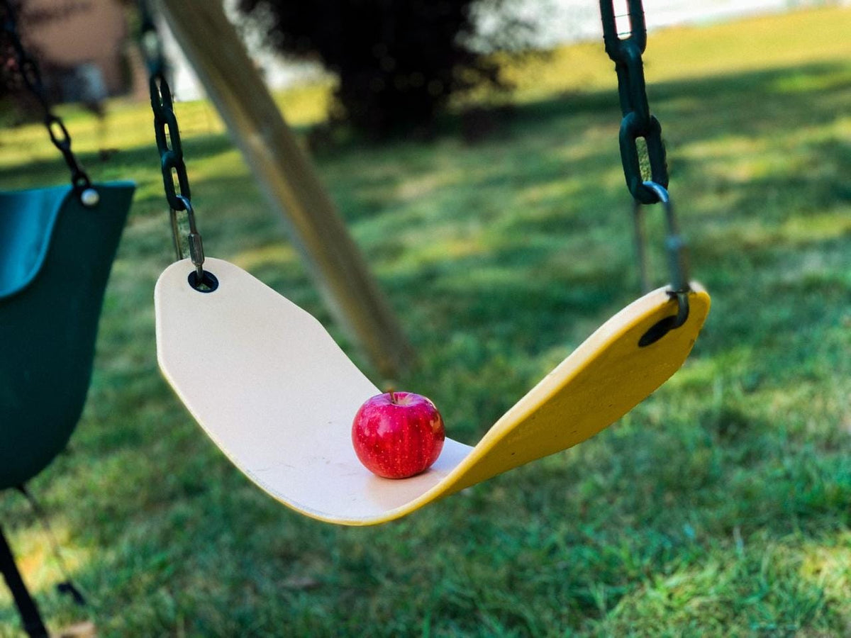 A red apple placed on a yellow swing set against a grassy background. Picked in Nystrom Orchard in Worthington Minnesota.